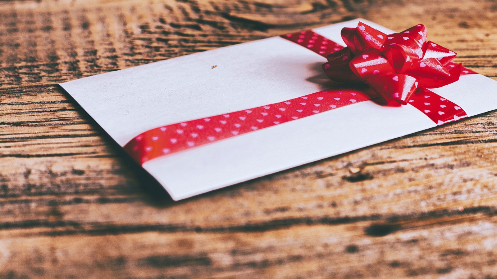 A white envelope with a red ribbon lies on a wooden table.