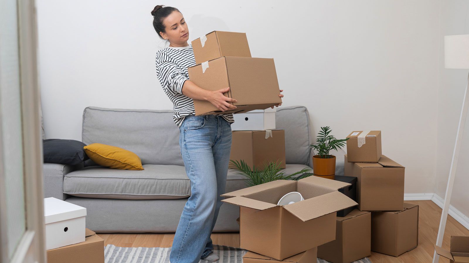 A woman is moving boxes in a living room.