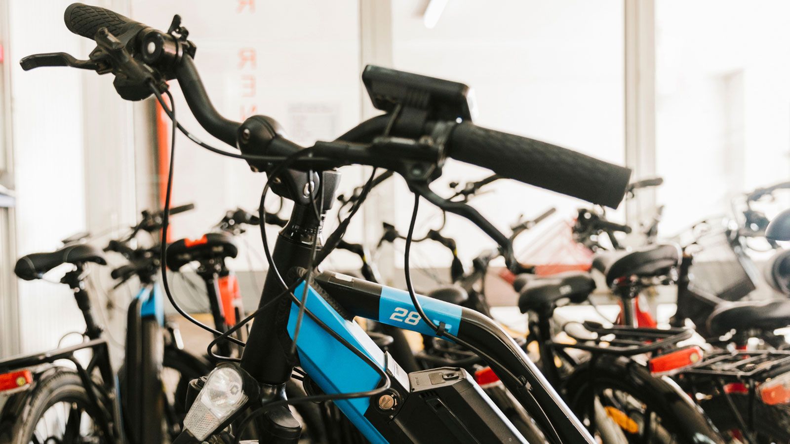 An electric bike with a blue frame and battery in a bike shop, with several other bikes in the background