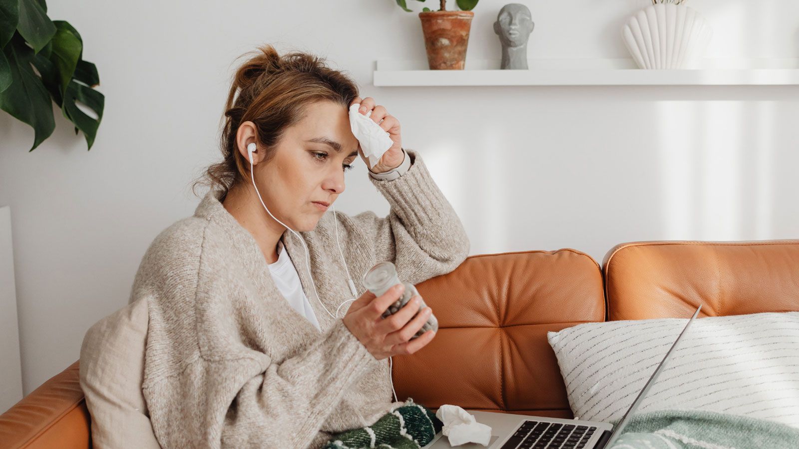 Person sitting on a brown leather sofa with a green and white striped blanket, holding a smartphone in their hand, with an open laptop on their lap.
