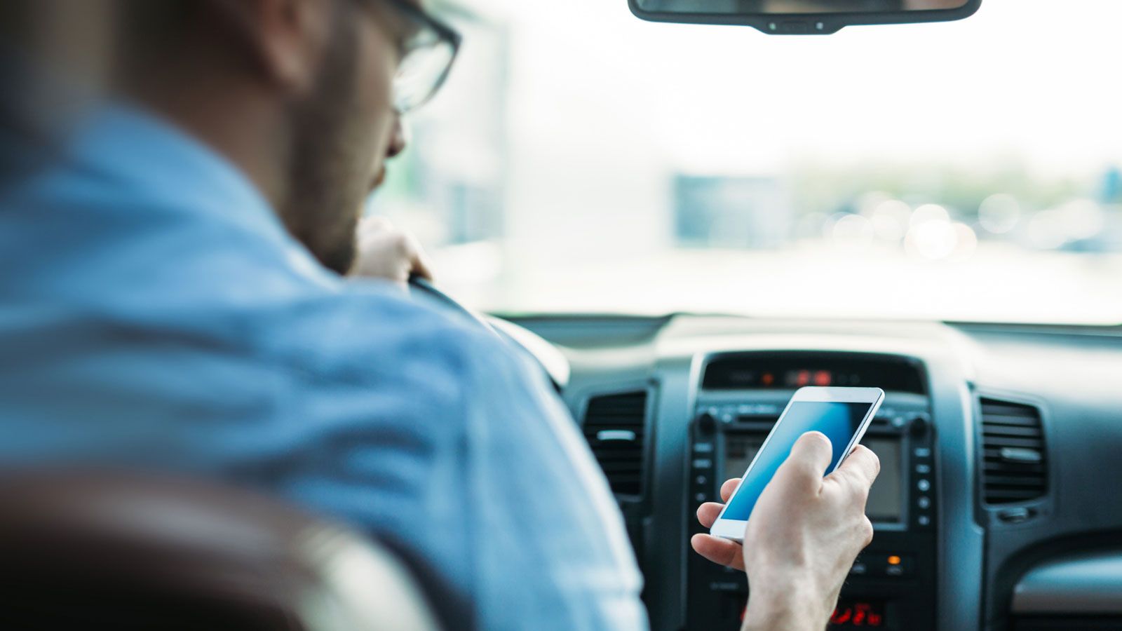 A man is using his cell phone while driving a car.