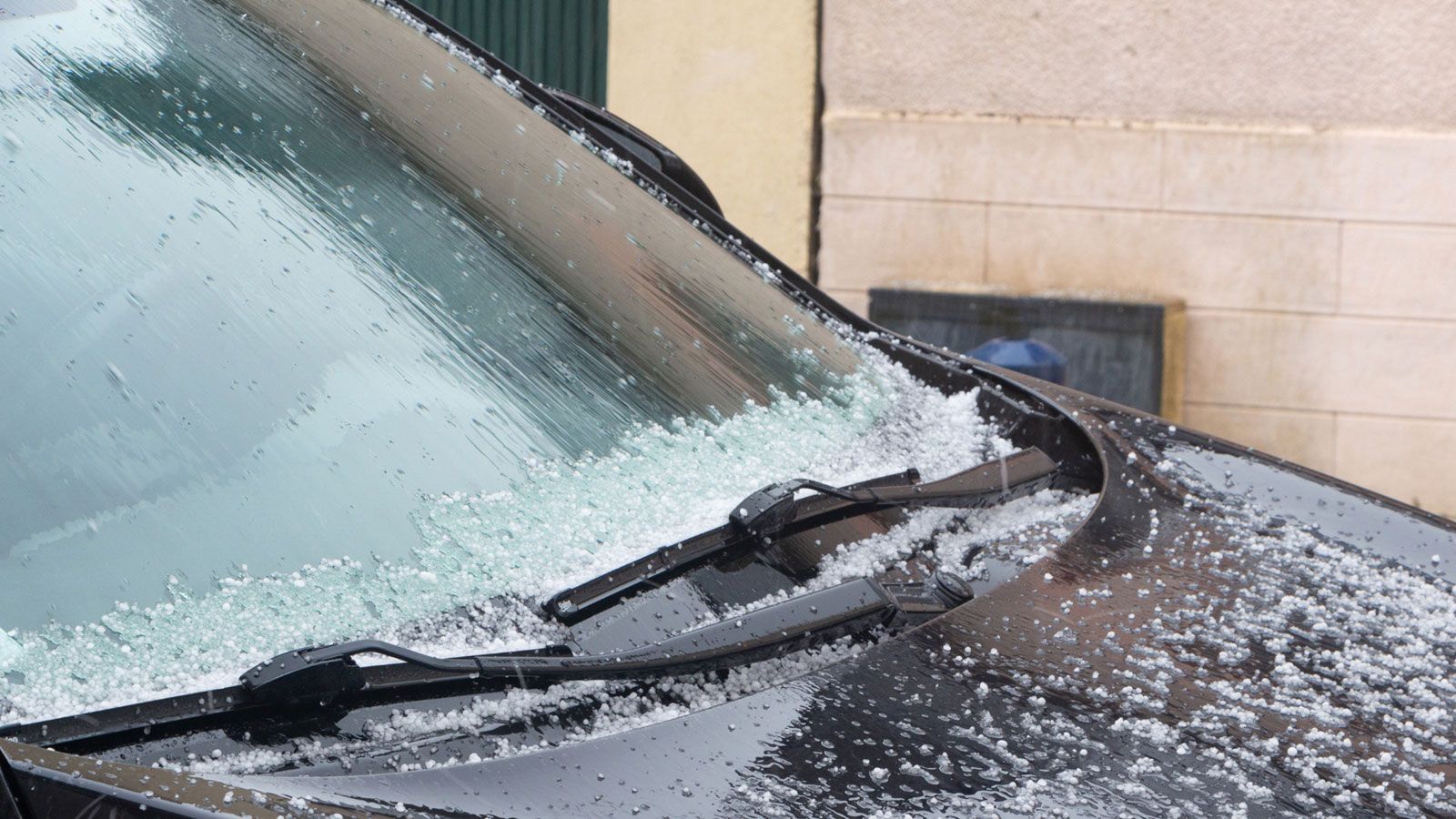 Close-up of the windshield and hood of a black car with frosted windshield wipers and patches of snow
