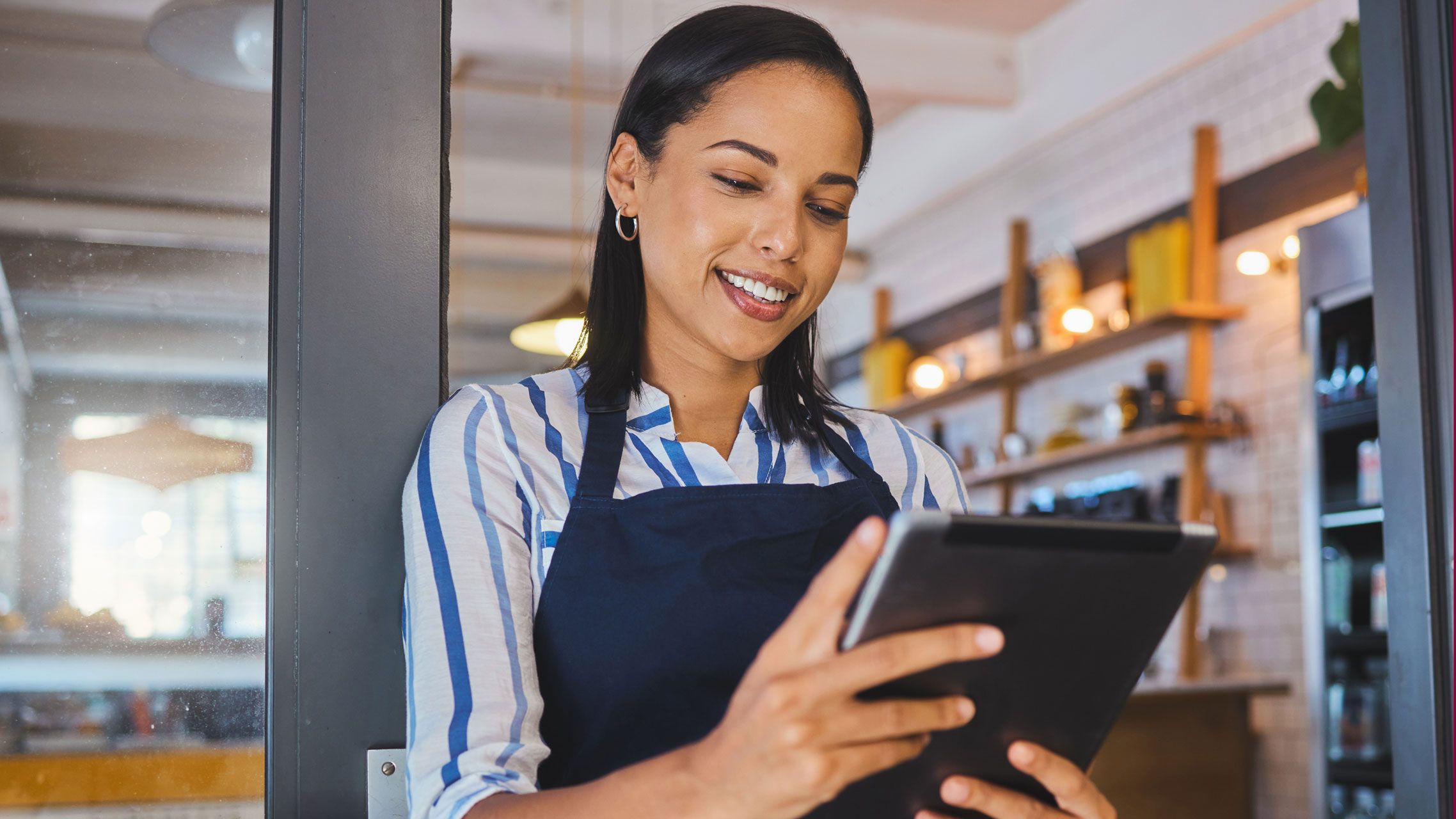 Startup, entrepreneur and female cafe owner working on a digital tablet to plan a budget. Proud, positive and successful leader checking inventory. Small business owner with door open to customers.