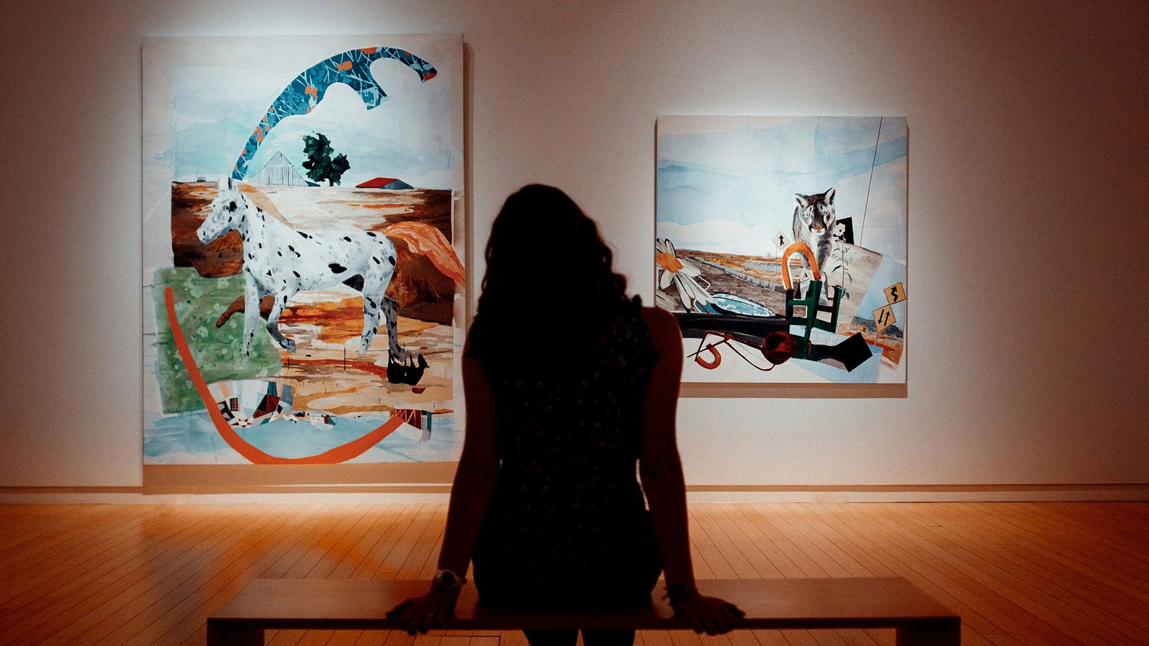 A woman is sitting on a bench in front of two paintings