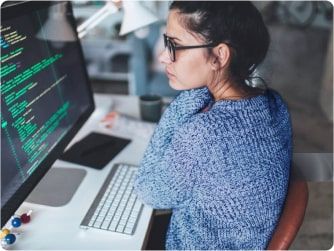 Junge Frau mit Brille programmiert an einem Computerbildschirm in einem modernen Büro.